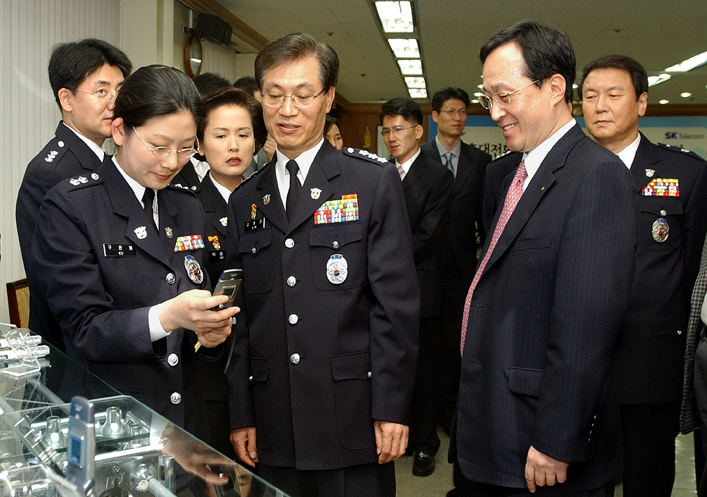 Hong Kweon Kim, vice-deputy director of the Korean National Police Agency (center), and Shin Bae Kim, president of SK Telecom, are shown signing the agreement for the Missing Child Finding Service Using Cellular Phones, and later observing a trial of the service performance. (A recovery of lost children service through the use of cellular Phones was activated on the third of May in a cooperative effort between SK Telecom and the Korean National Police Agency.)